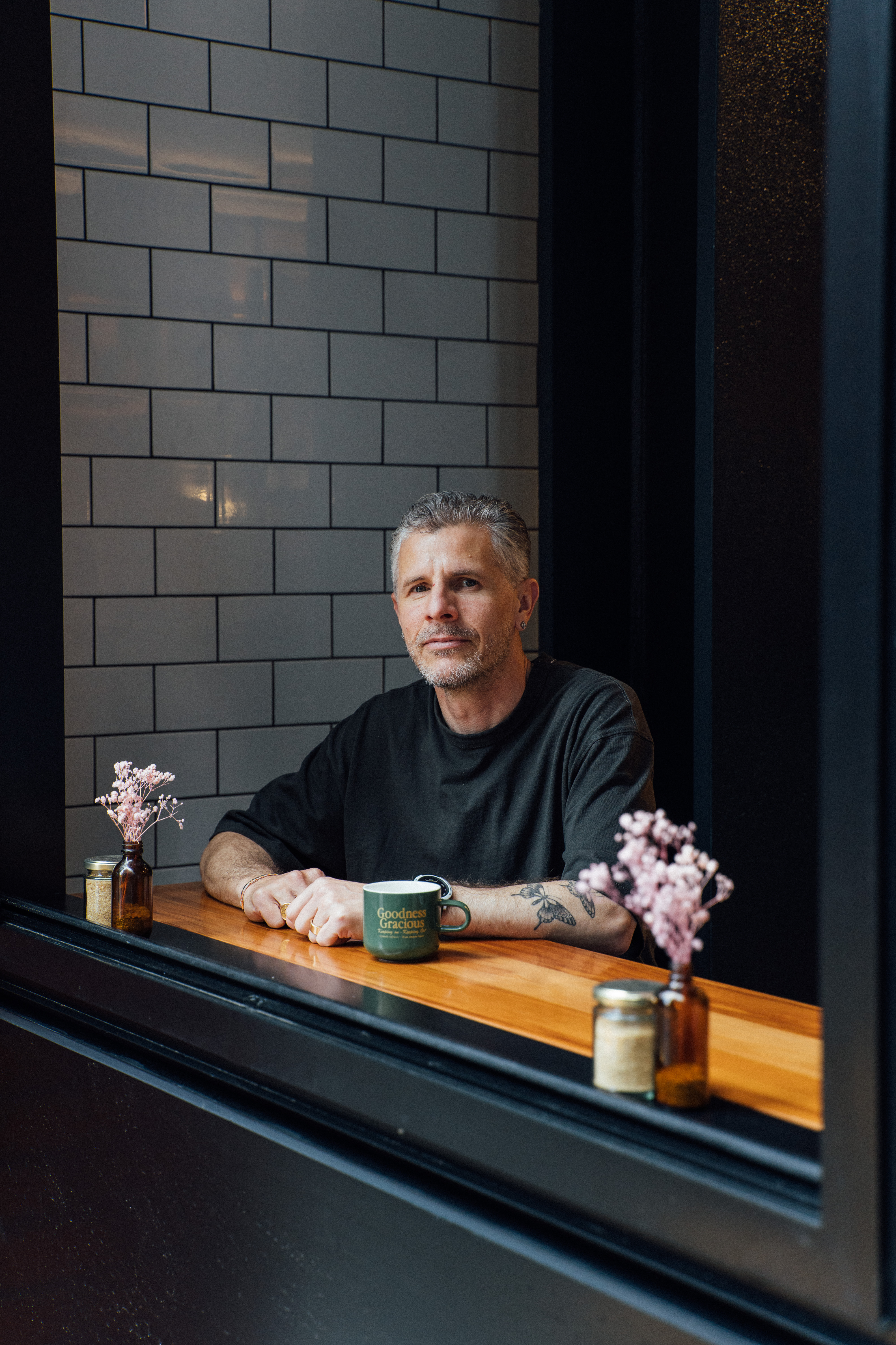 Greg Cornes at Goodness Gracious, mug in hand by the tiled window
